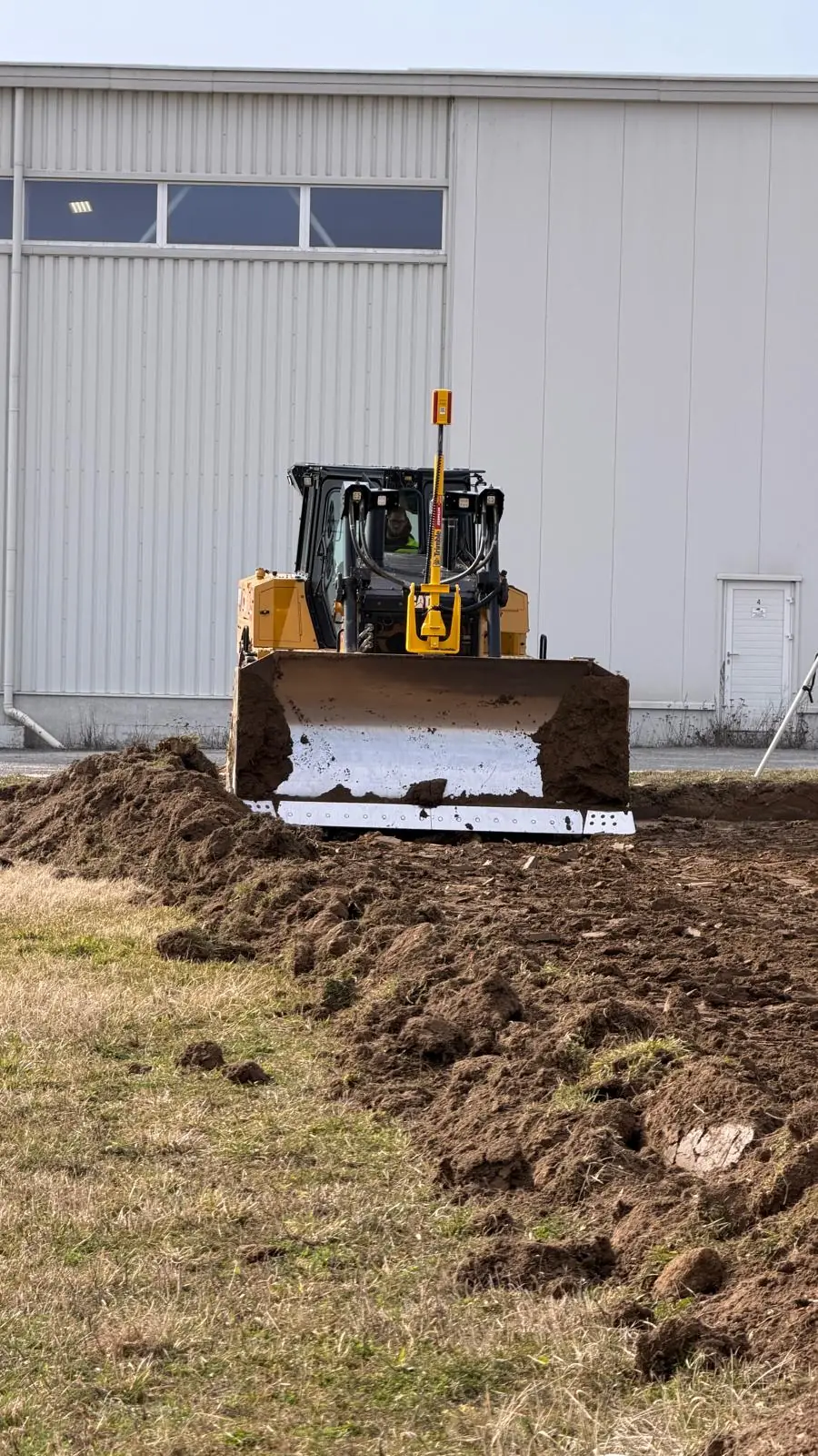 Dozer CAT s Trimble nivelací při skrývce ornice u haly
