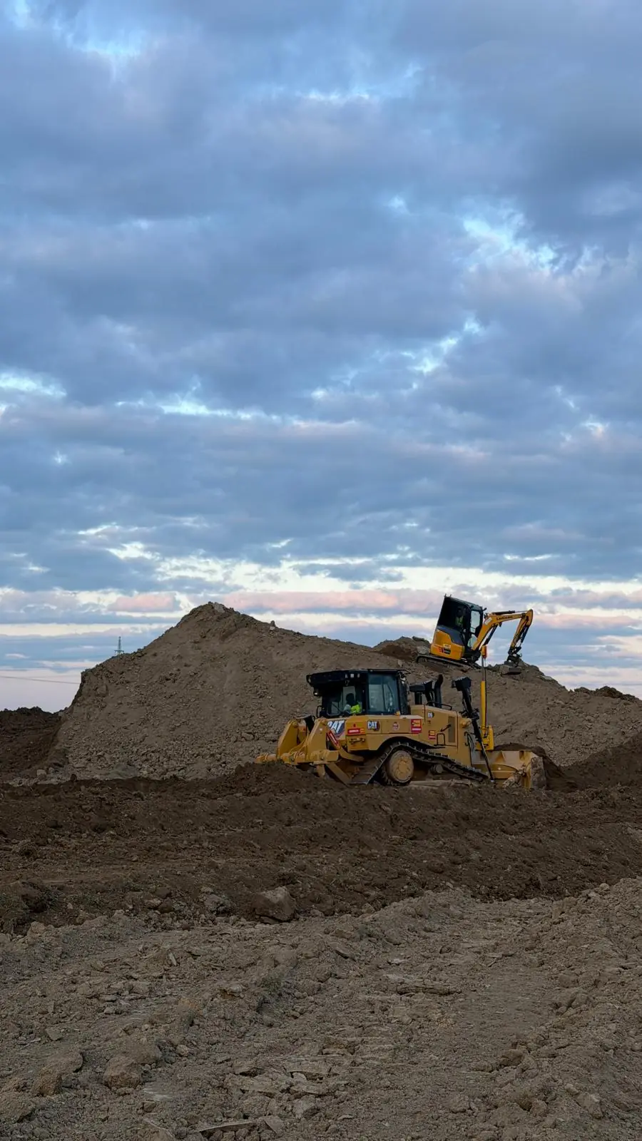 Dozer a rypadlo při přemísťování výkopku za soumraku